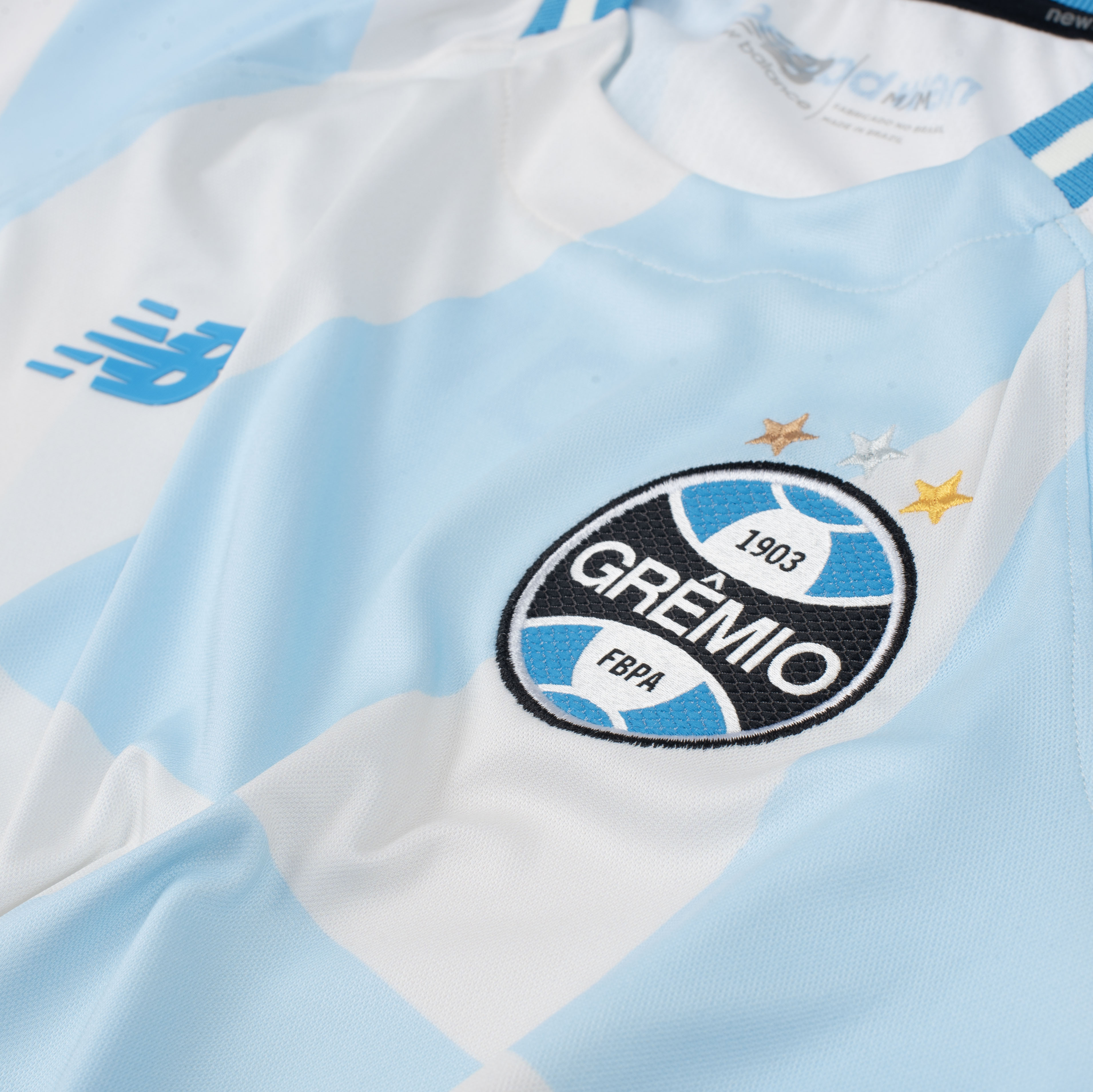 Detalhe lateral da camisa feminina Grêmio New Balance com escudo e listras em degradê